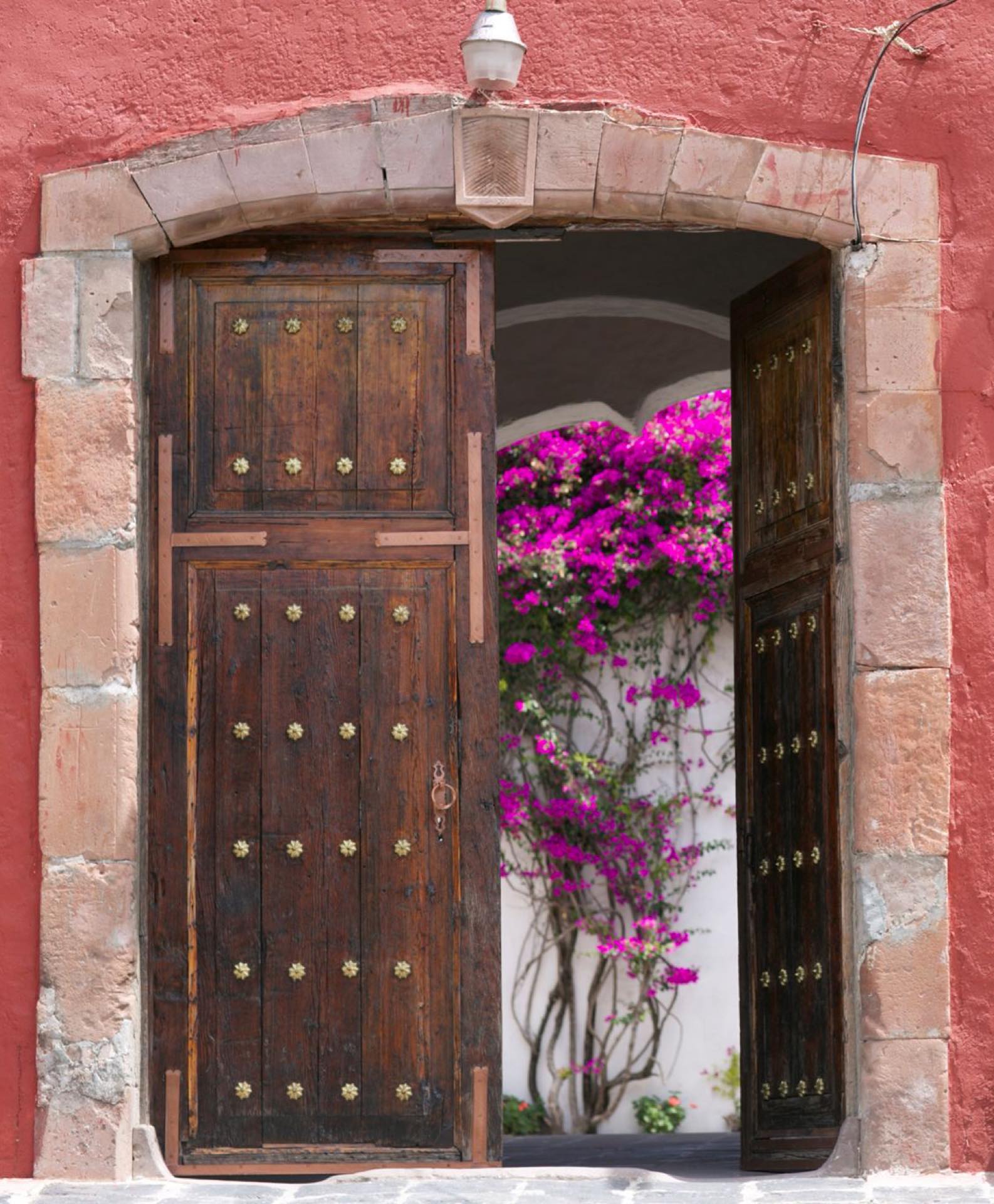 Portón de cantera con clavos de bronce y bugambilia al fondo